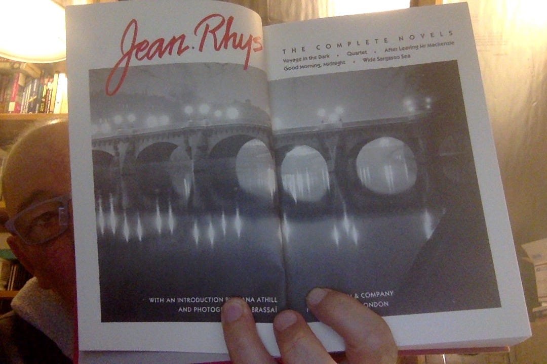 Photo of some guy whose face is partially obscured by the book he's holding open: Jean Rhys, The Complete Novels. The frontispiece is a 2-page spread with photo of a bridge over a river at night, in fog, illuminated by blurry streetlights, which are reflected in the still water below.