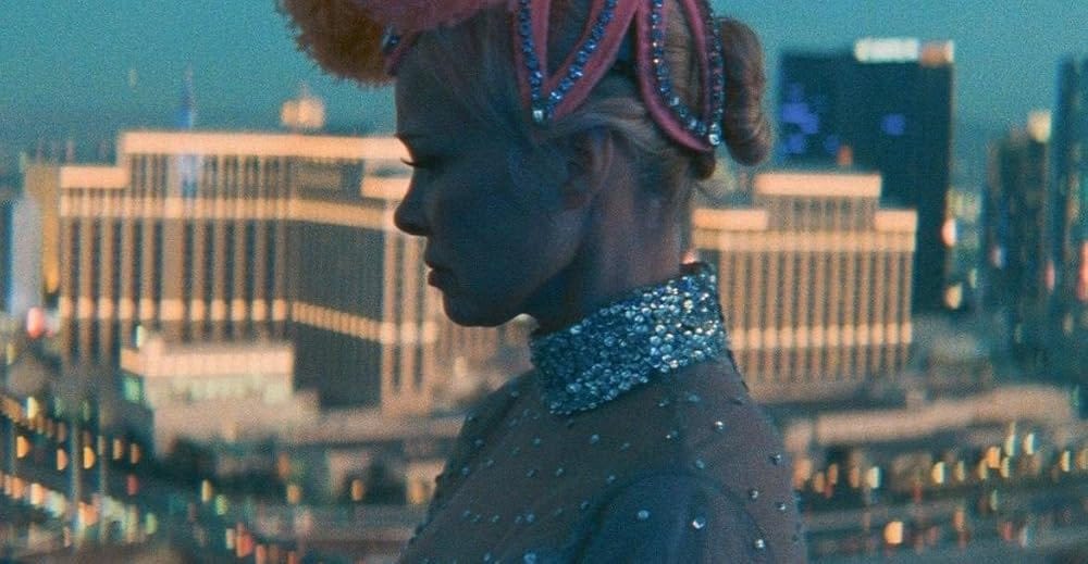 Pamela Anderson in "The Last Showgirl", dressed in a Vegas showgirl costume as she looks over the Las Vegas strip sadly.