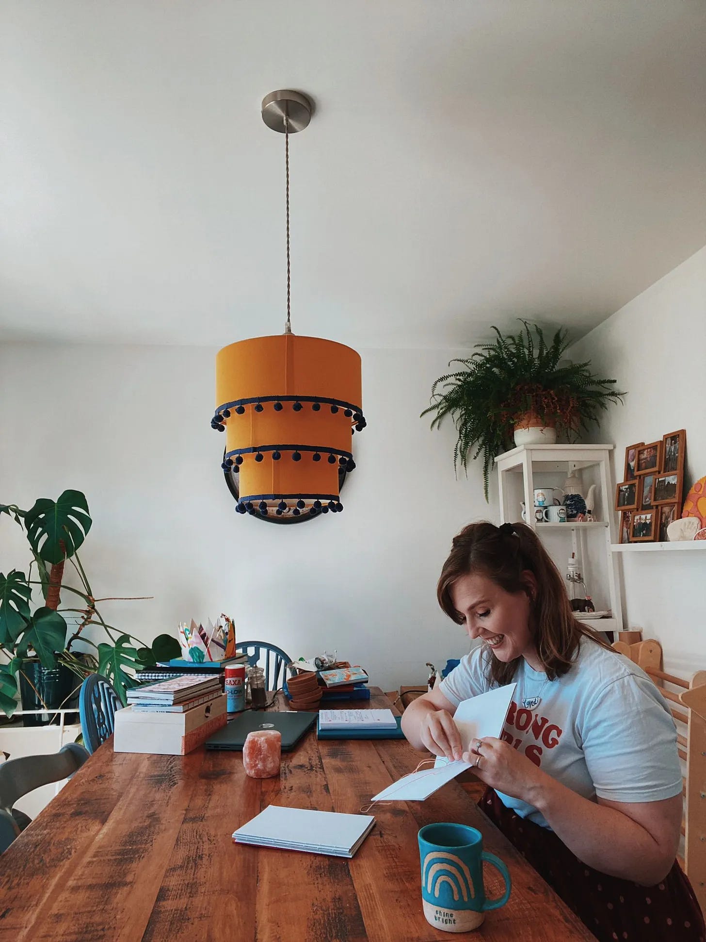 Zoe sits at a table with a notebook and rainbow mug smiling.