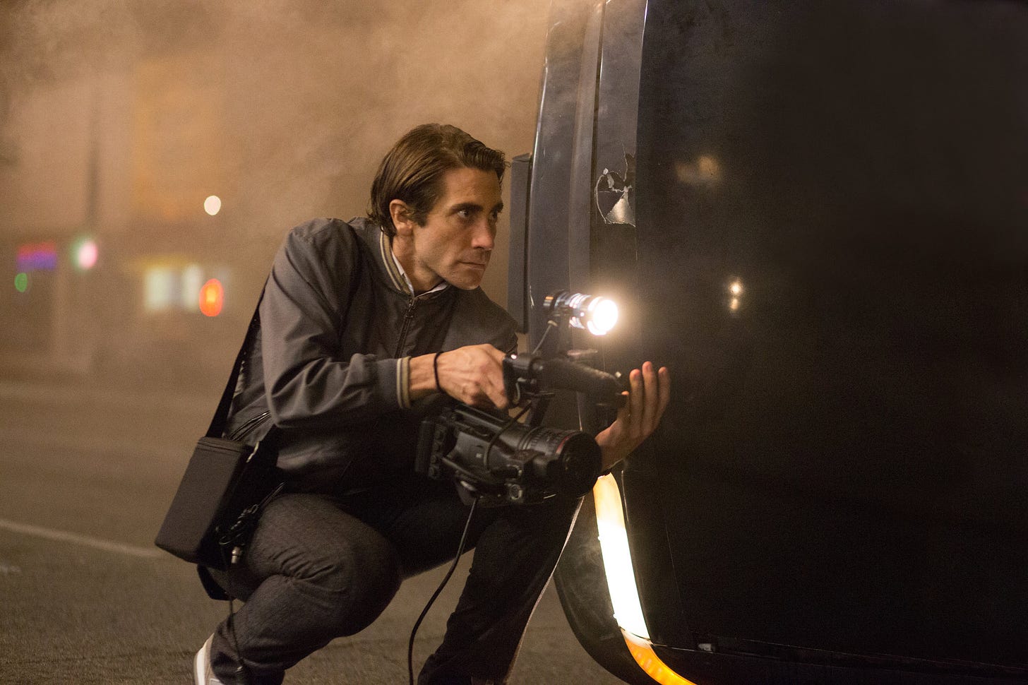 Jake Gyllenhaal in Nightcrawler, kneeling near a car accident with a digital video camera to get a shot.