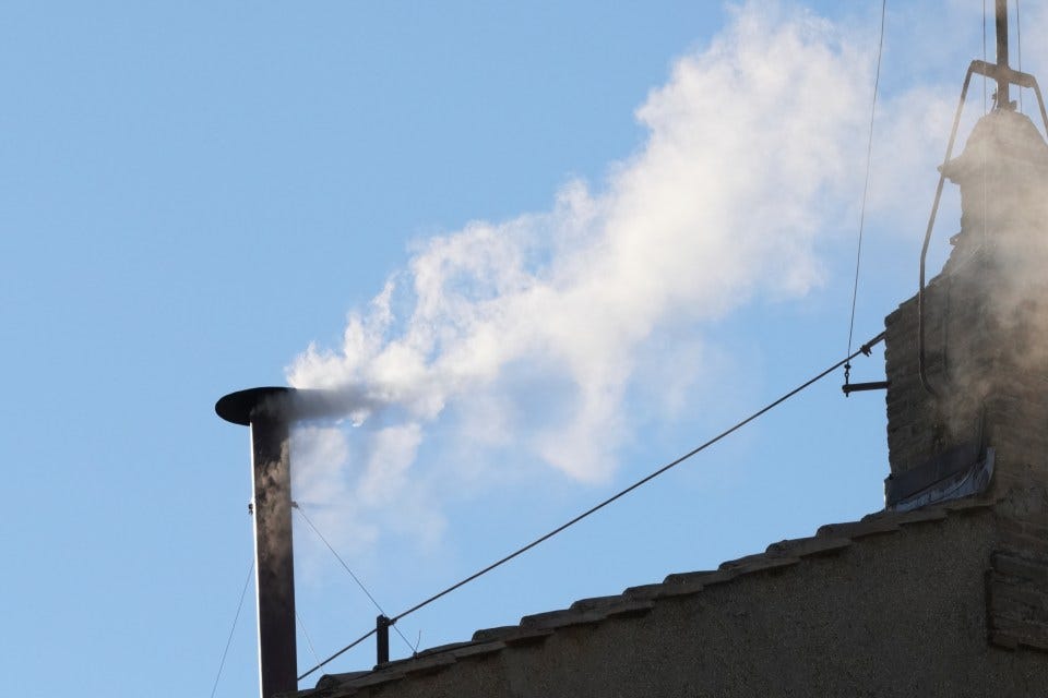 White smoke billowing from a chimney against a blue sky.