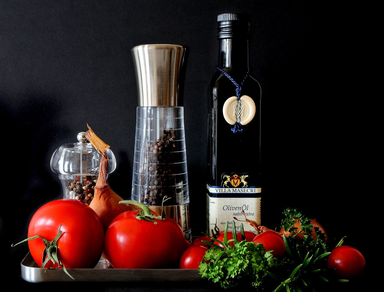 tomatoes and herbs next to a pepper mill and olive oil jar