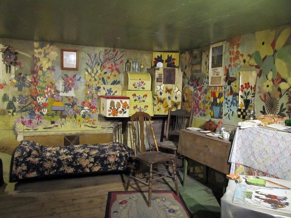 El interior de la casa de Maud lewis, en la estancia se puede ver la mesa, una cama, una silla y todas las paredes y armarios con dibujos.