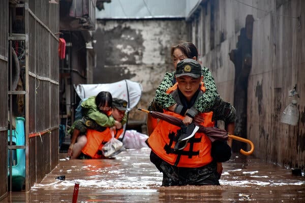 Two residents ride on the backs of rescuers wading through knee-deep water.