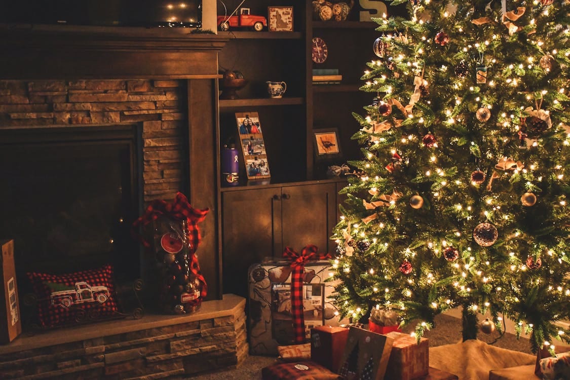 Free Warm holiday scene of a decorated Christmas tree with gifts by a cozy fireplace. Stock Photo