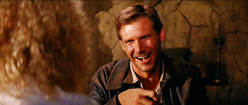 Harrison Ford as Indiana Jones wearing a wicked smile while appearing to eat popcorn