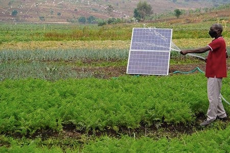 Un paysan arrose son champs, la main gauche tenant un petit panneau solaire amovible