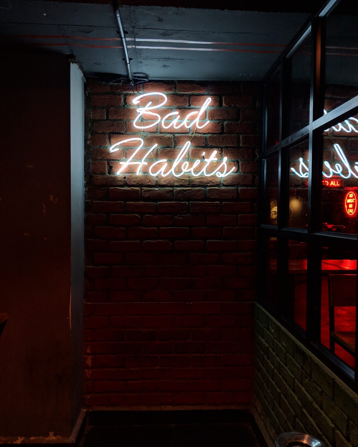 A diml lit brick wall with a neon sign saying “Bad Habits”