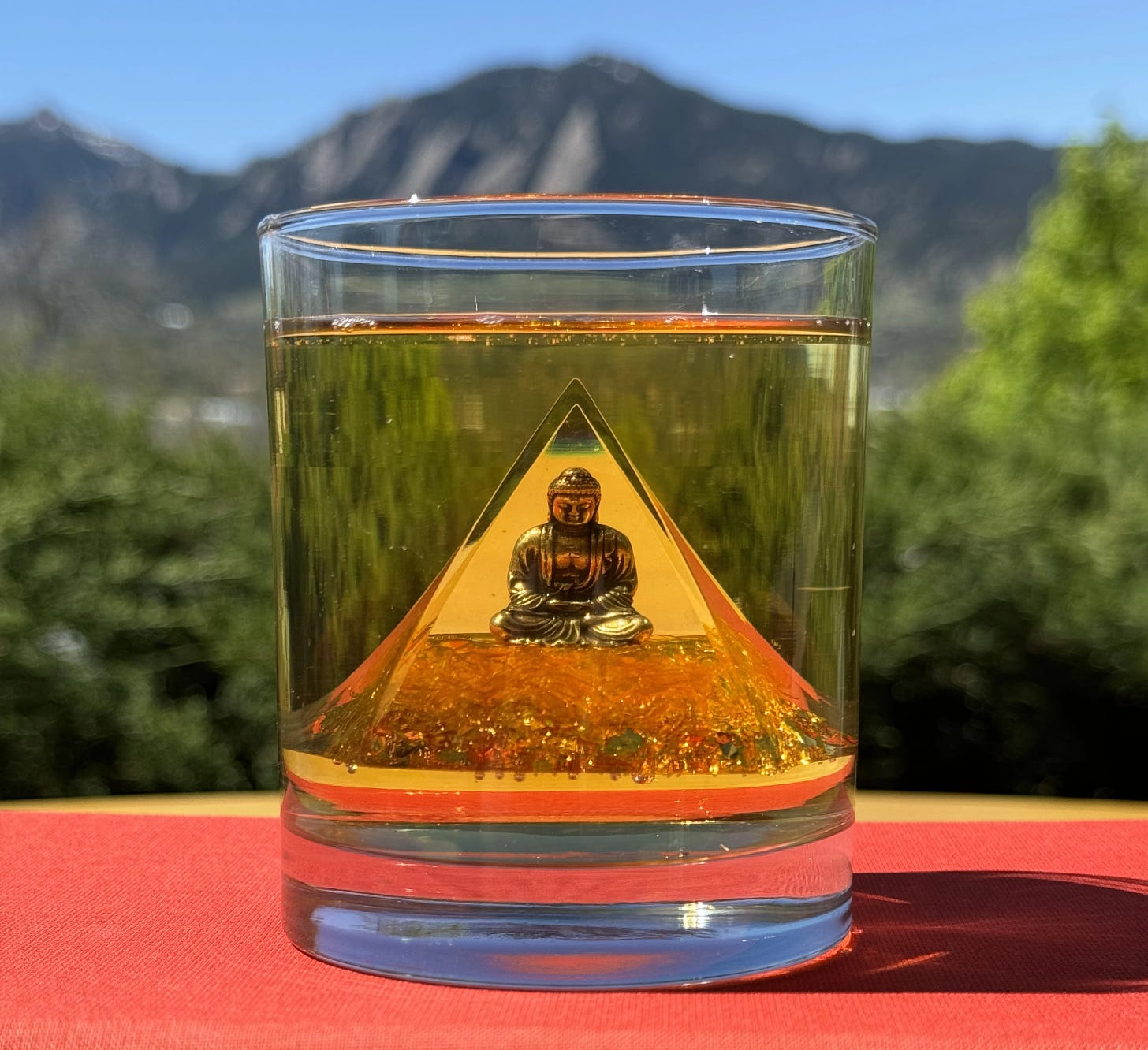 A Buddha statue submerge in a glass of yellow liquid