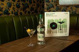 A green leather vintage-looking cocktail lounge booth with a martini glass, a bottle of gin, and a record on the table.
