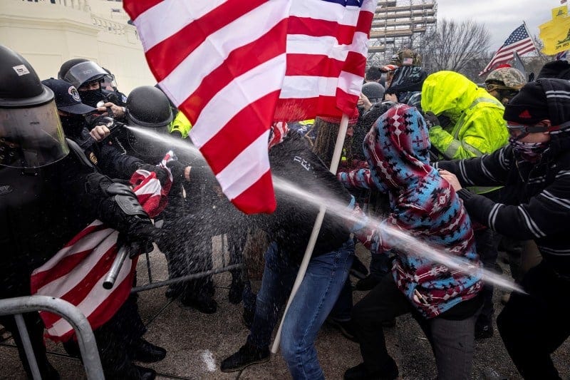 Police in riot gear clash with protesters holding American flags outside the U.S. Capitol.