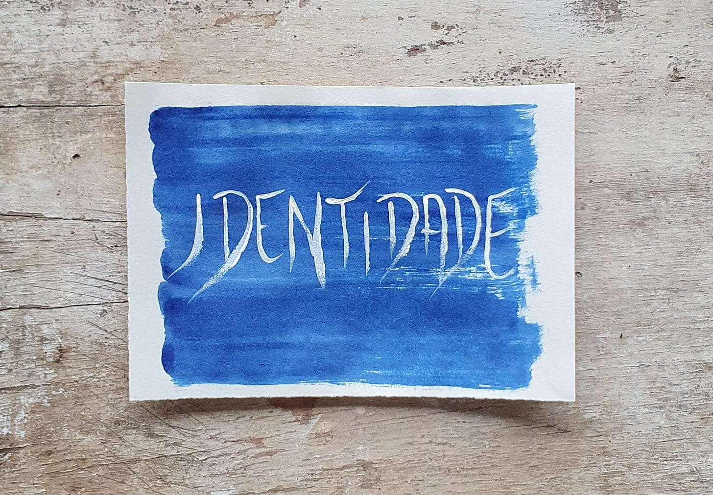 Fotografia de um papel pintado de azul escuro, com a palavra "Identidade" escrita, sobre um fundo de madeira 