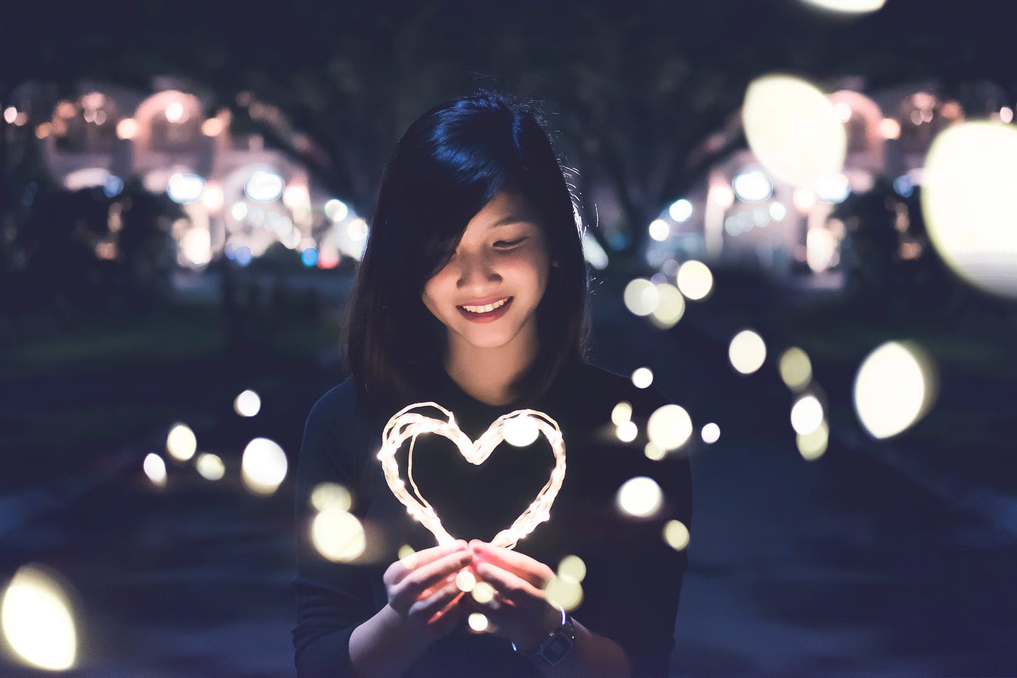 A woman holding a heart made of light, surrounded by light sparkles.