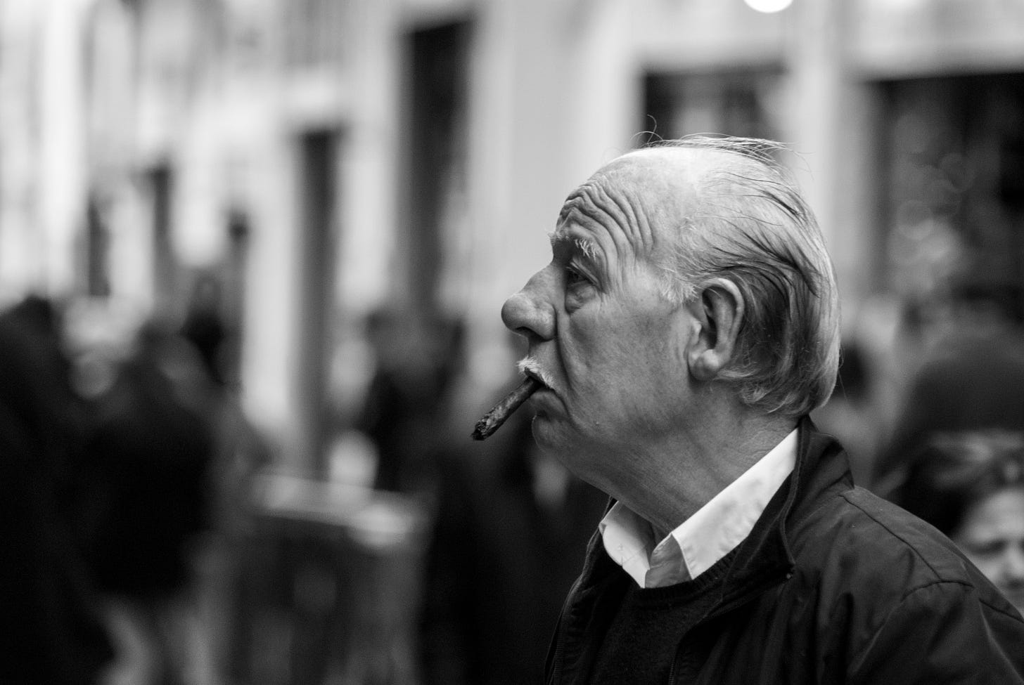 A black and white photograph of an elderly man, in profile, with a cigar dangling from his mouth.