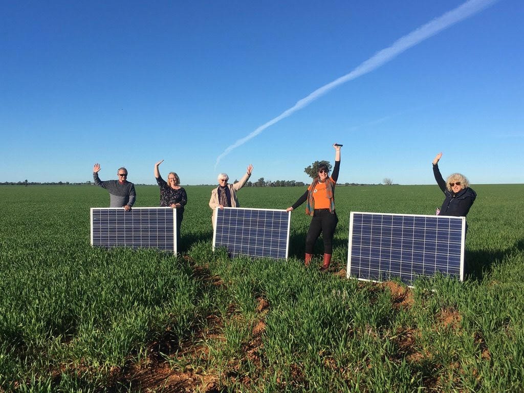 Photo of 5 people standing in a field holding solar panels