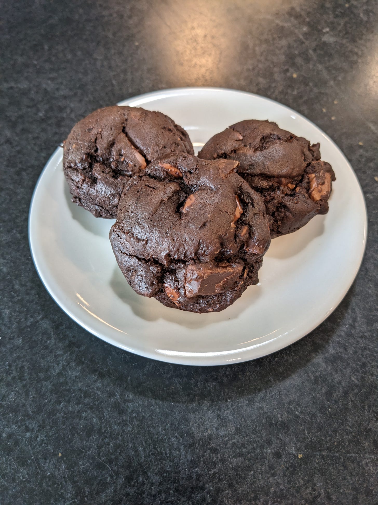 A small white plate holding three chocolate cookies
