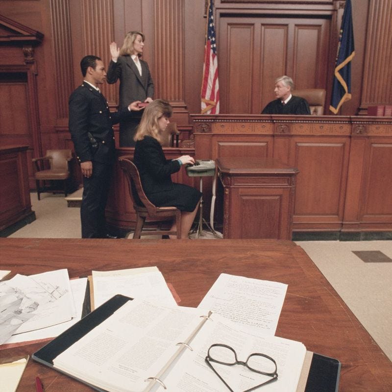 A courtroom with three people in suits, one is typing.