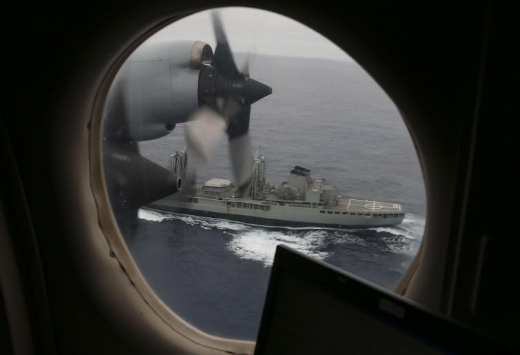 A Royal Australian Air Force AP-3C Orion flies past a warship as they search for missing Malaysian Airlines flight MH370 debris or wreckage in Southern Indian Ocean