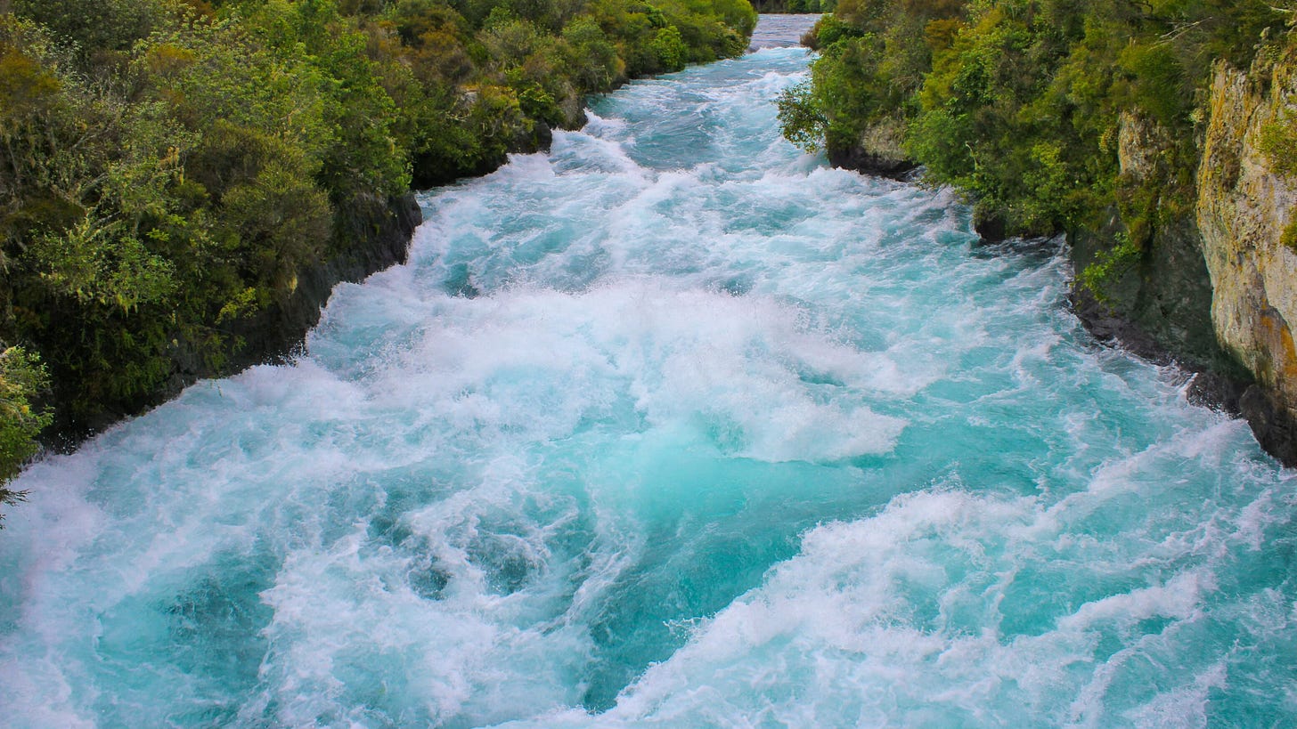 A roaring river in crystalline turquoise and white cuts a swath through a lush forest.
