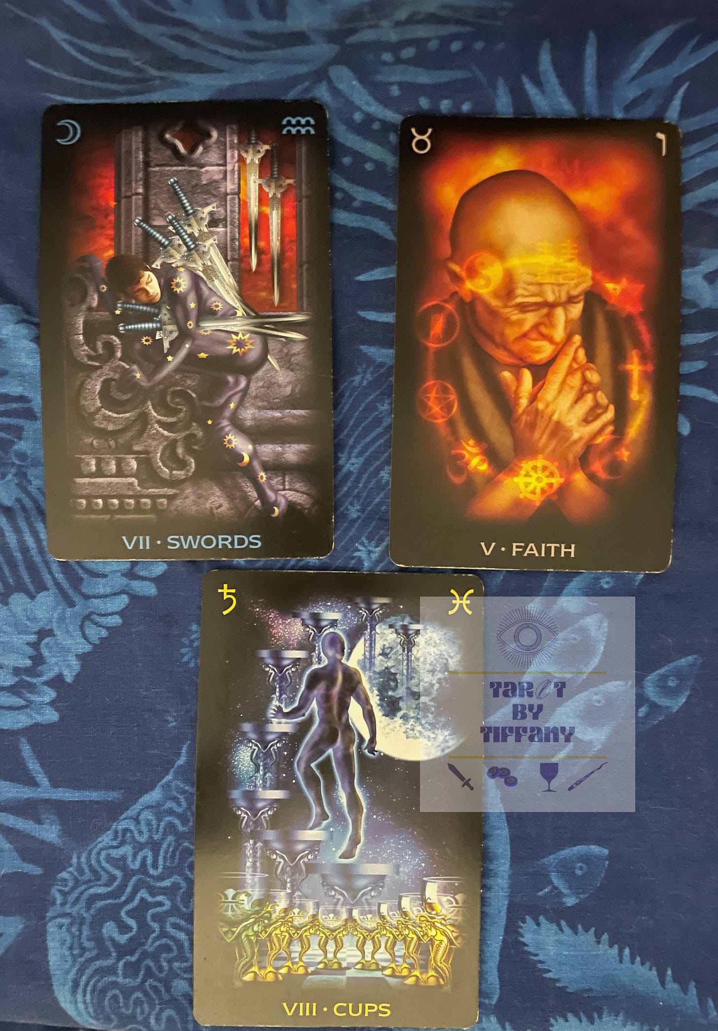 3-card reading using the Tarot of Dreams by Ciro Marchetti. Cards are laid out on a blue cloth with an sea life motif in light blue. Top two cards (left to right): 7 of Swords and Hierophant (Faith). Bottom card: 8 of Cups.