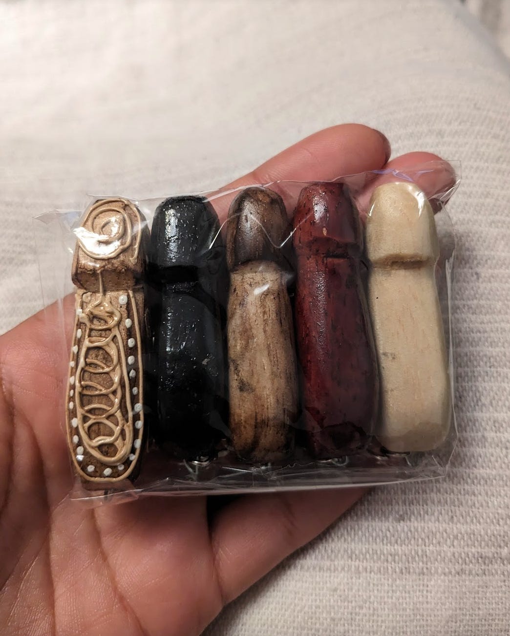 A hand holds 3 penis shaped key chains that are in a range of colors from red to brown to black