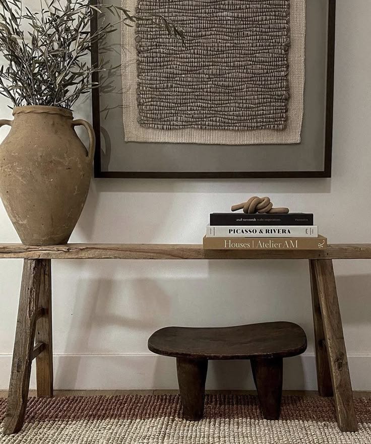 This may contain: a wooden bench sitting in front of a wall with a vase on top of it This may contain: a wooden bench sitting in front of a wall with a vase on top of it
