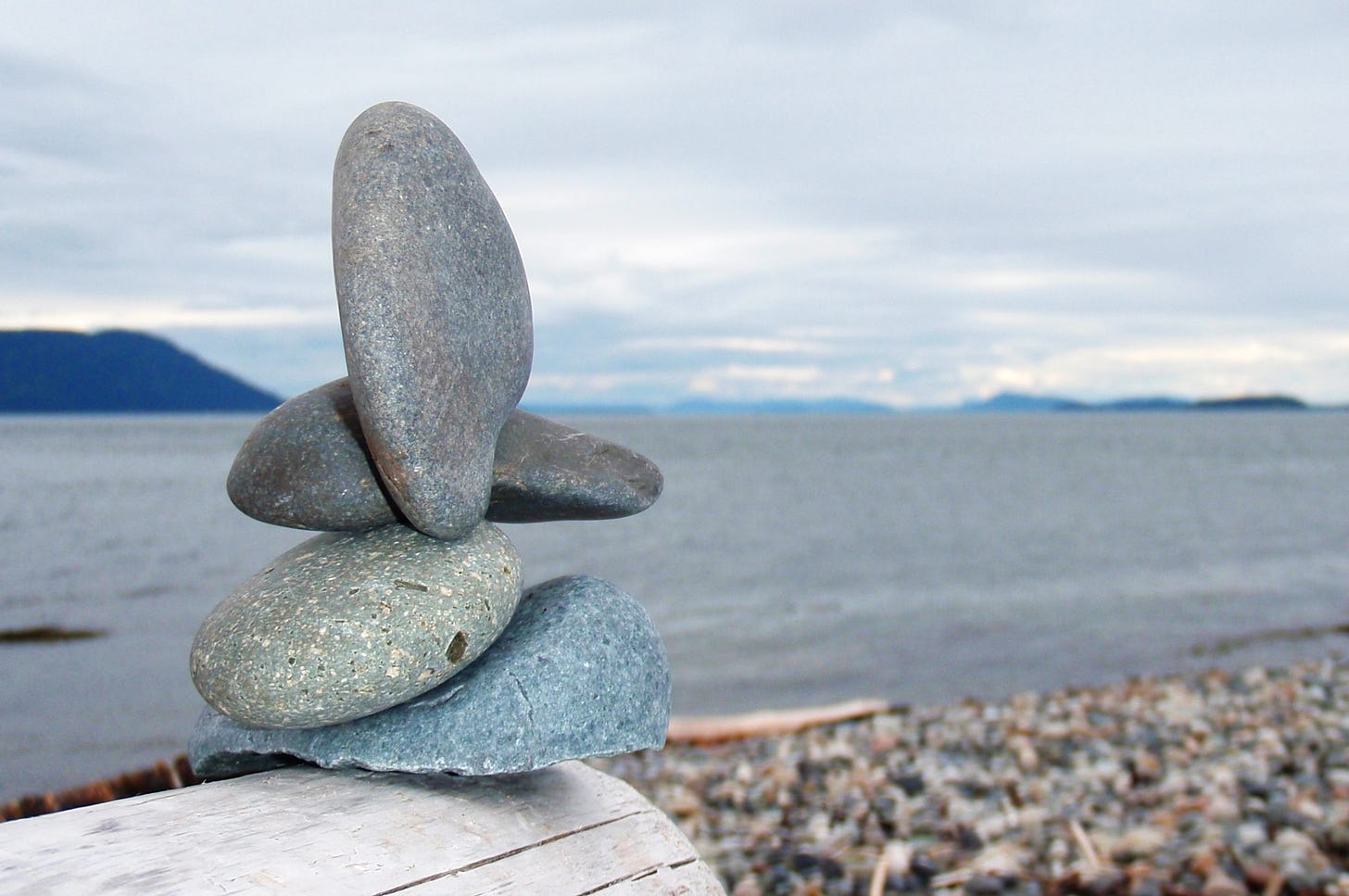 A cairn of smooth stones rests on driftwood against a view of the horizon.