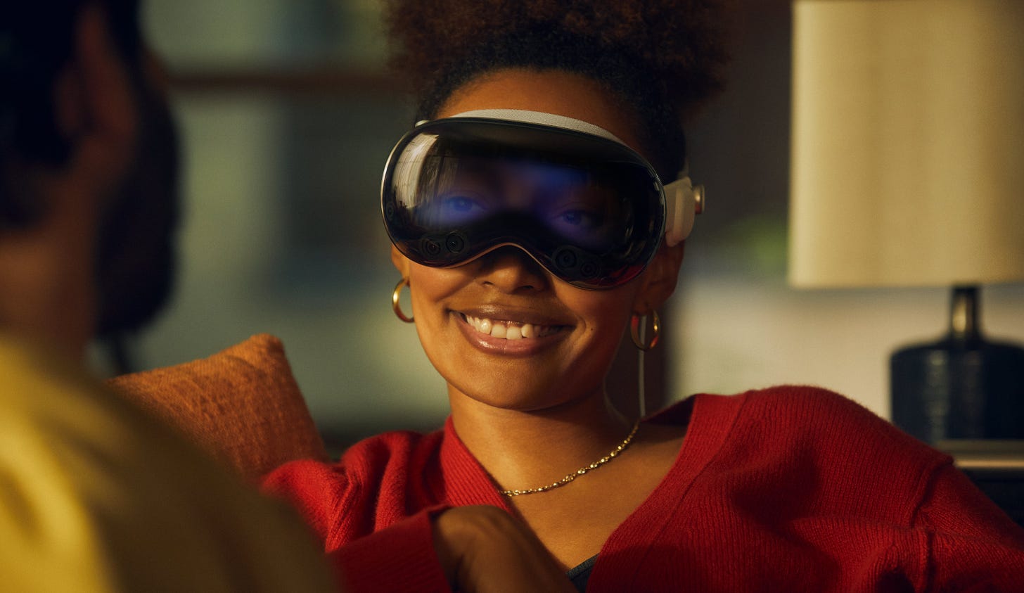 A woman unnervingly smiles at someone just off camera, while wearing the Apple Vision Pro, her gaze faintly obstructed by a haze of digital content.