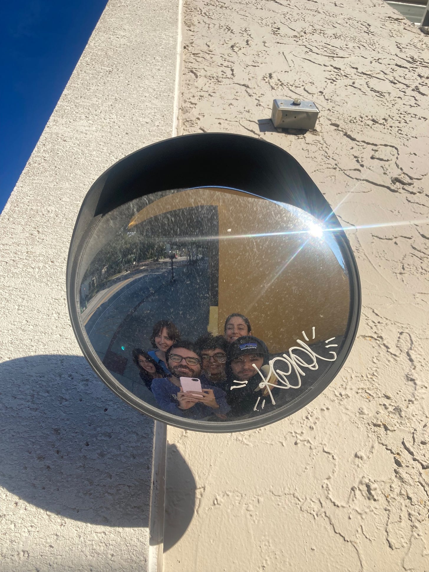 Jake and friends smile in the reflection of a convex mirror