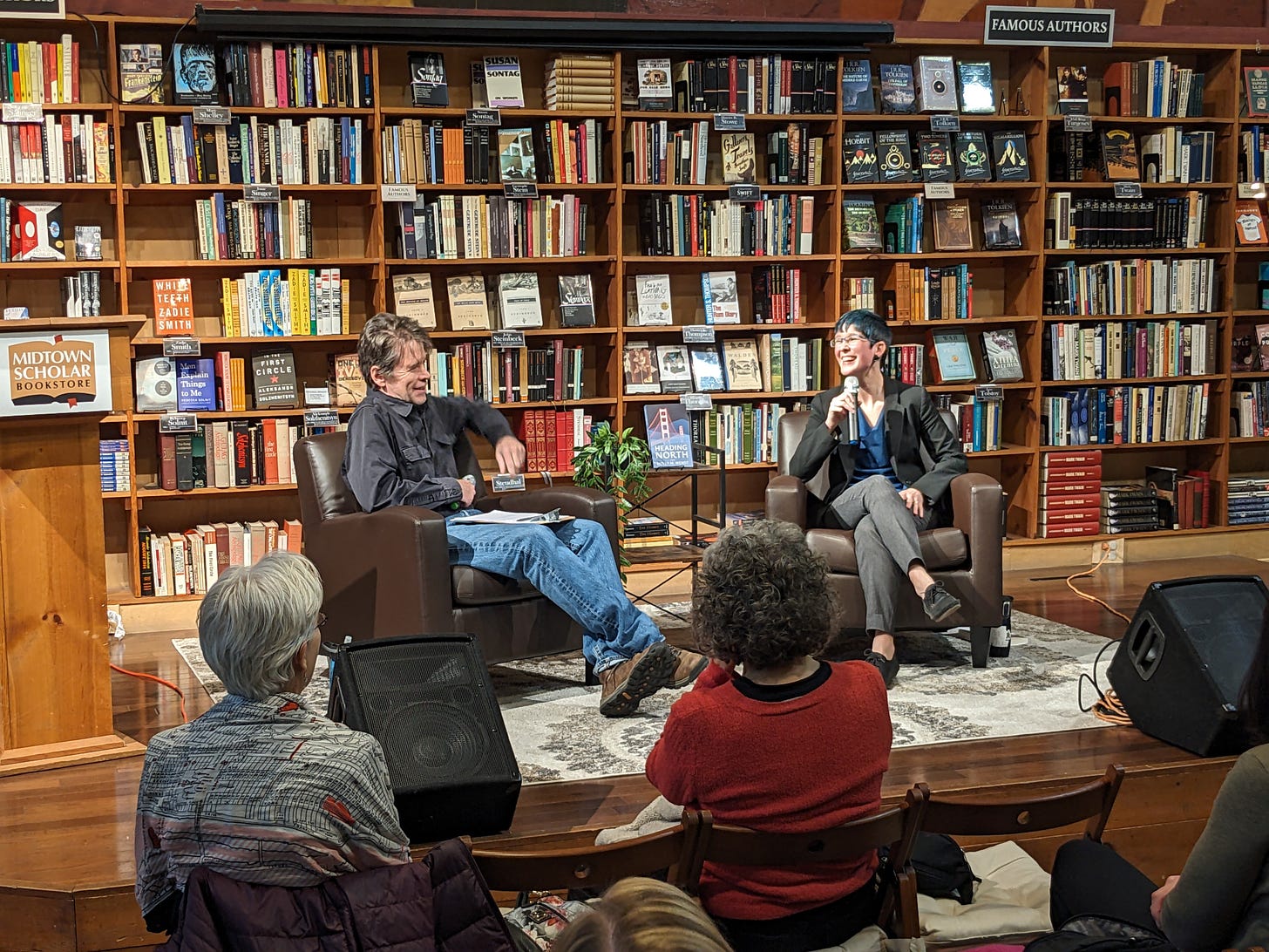 A photo of authors Curtis Smith and Holly M Wendt in conversation at Midtown Scholar bookstore. Both writers are seated in front of a wall of books.