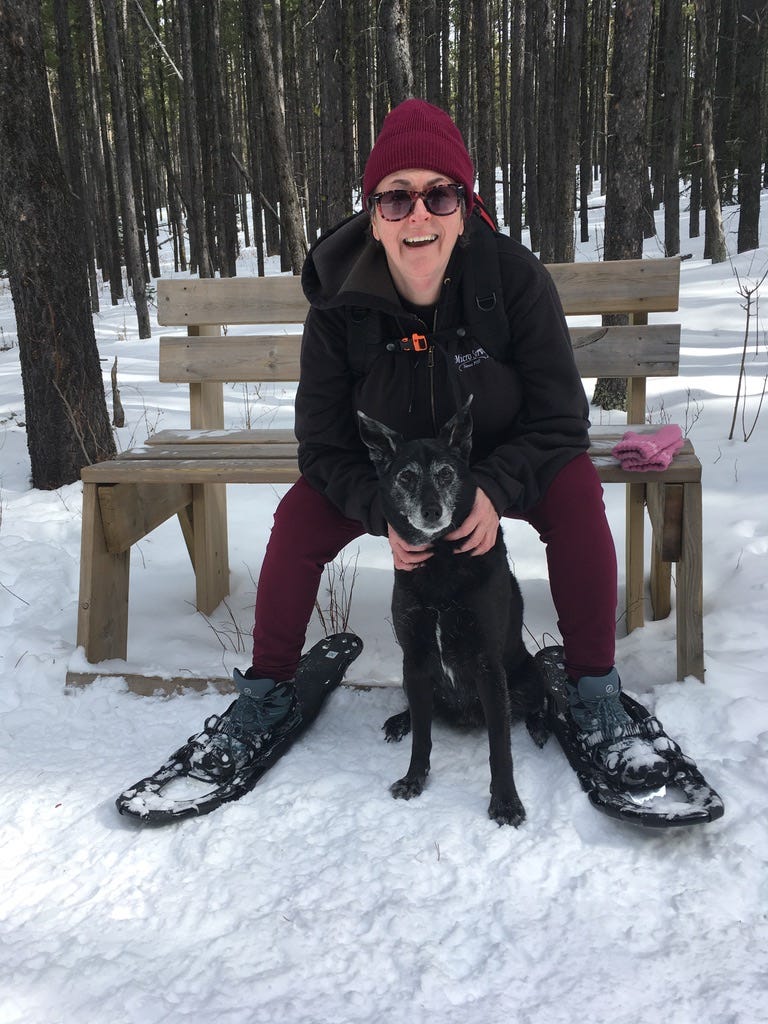 Woman in snowshoes sitting on a bench with a dog.