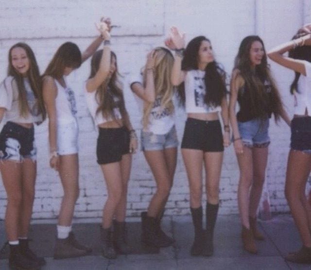 This may contain: a group of young women standing next to each other in front of a brick wall