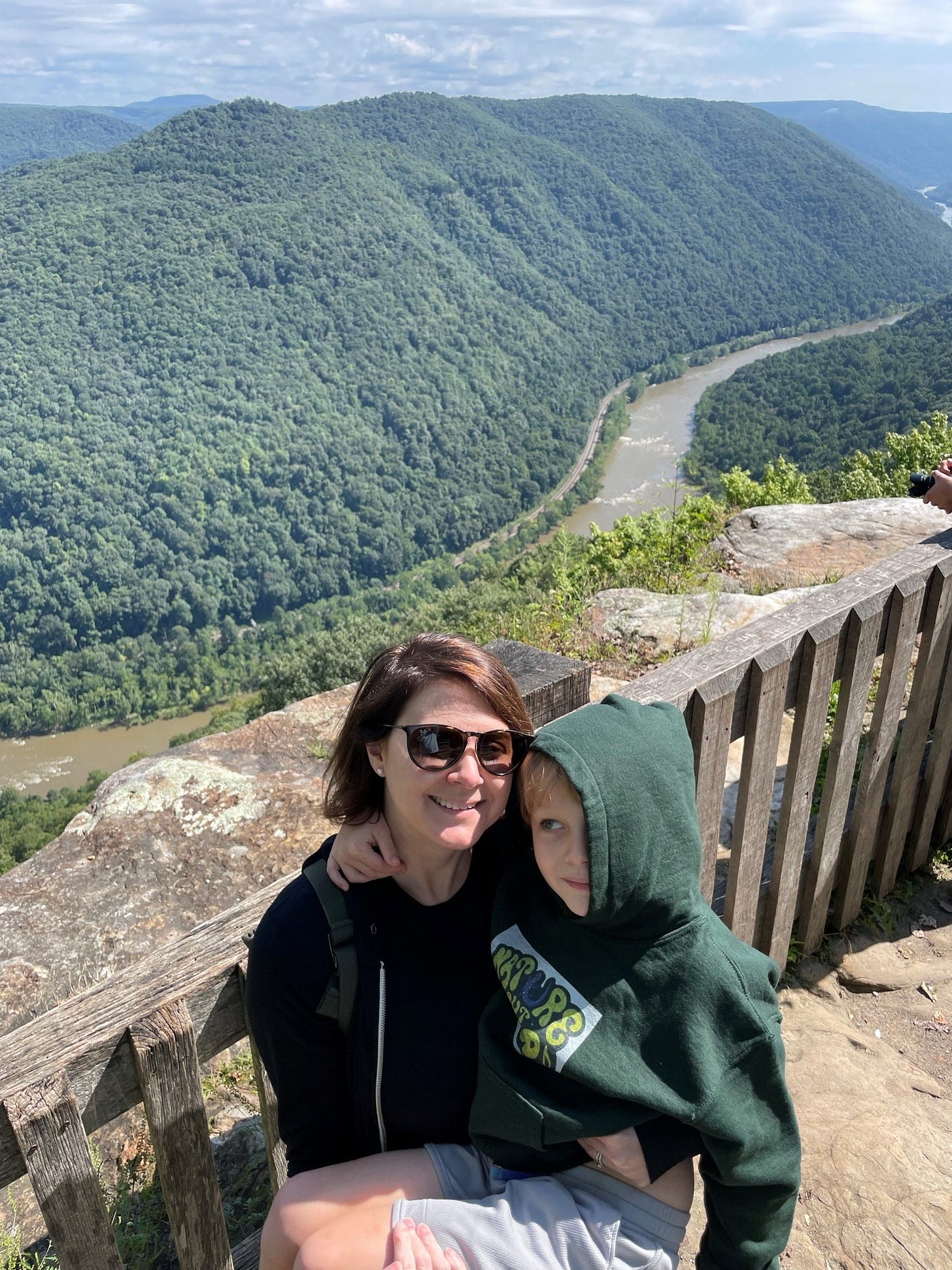 Woman holding small child, background of big view of forested mountain and river