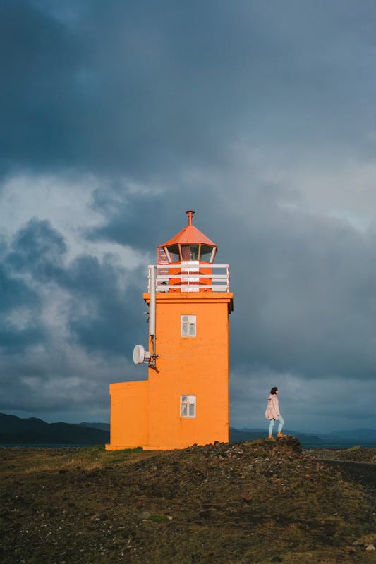 One lighthouse, one woman, both standing on the shore in Iceland. 