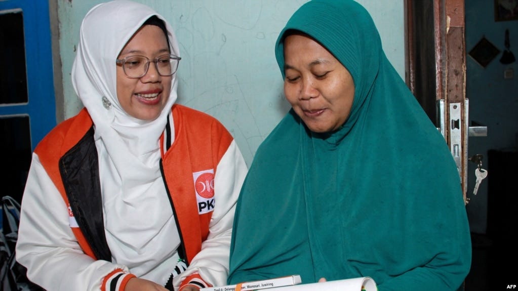 Lingga Permesti, left, a legislative candidate for Indonesia's Islamic Prosperous Justice Party (PKS), presents a calendar to a resident during house visitations ahead of the election in Klaten, Central Java, Jan. 18, 2024.