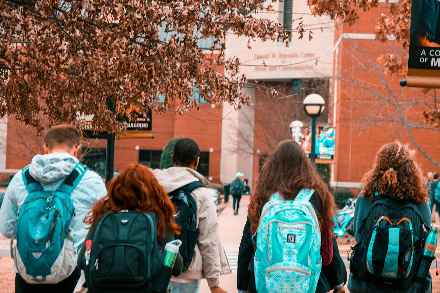 Students walking into a classroom building wearing backpacks in what appears to be fall.