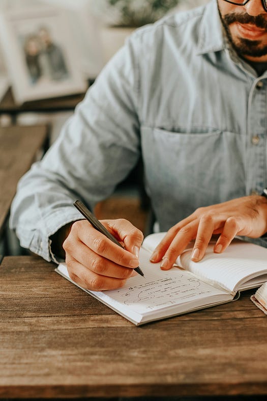 Man writing with a pen at a desk in a Journal.