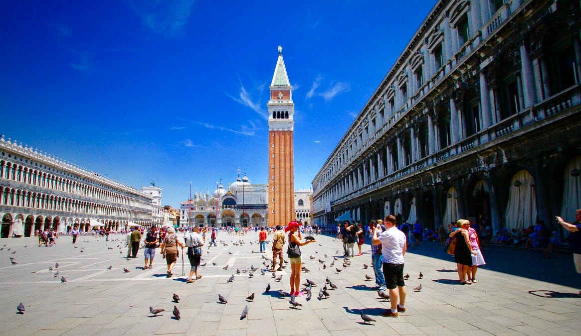 A group of people in a plaza with Piazza San Marco in the background

Description automatically generated