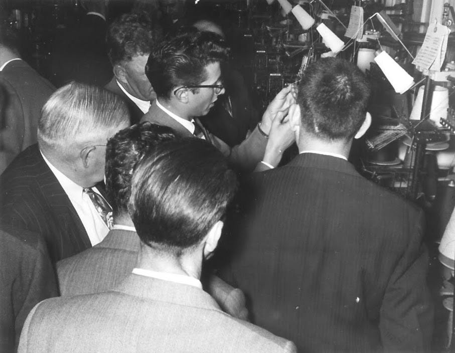 Back of men's heads as they look at hosiery machinery