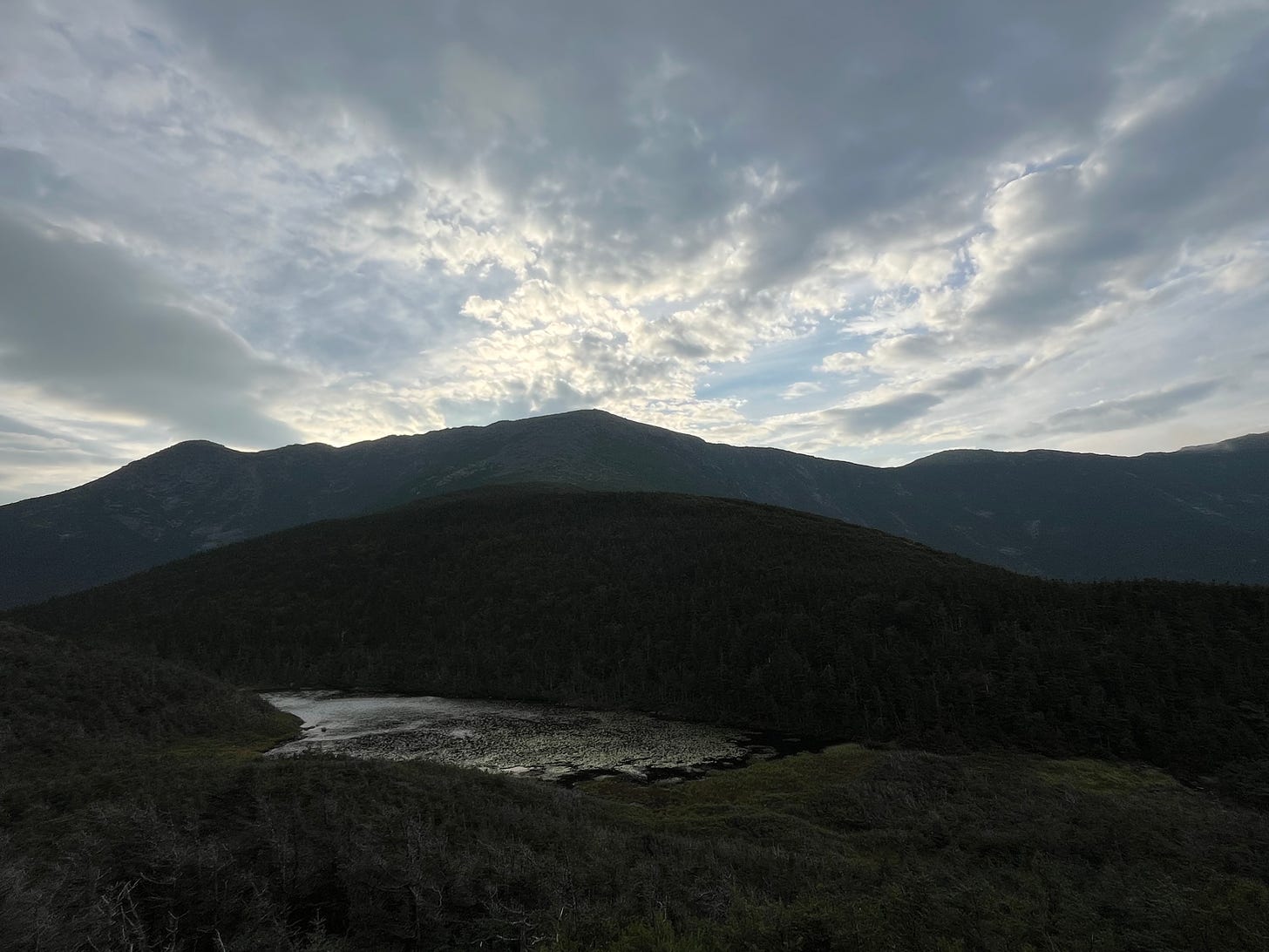 View of the small pond in front of Greenleaf Hut, and the Franconia Ridge behind it, in dark, dramatic lighting.