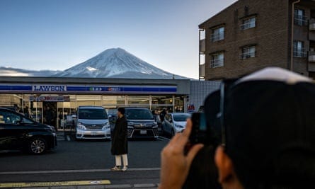 A tourist posing in front of a Lawson convenience store with Mount Fuji in the background, in the town of Fujikawaguchiko, Yamanashi prefecture