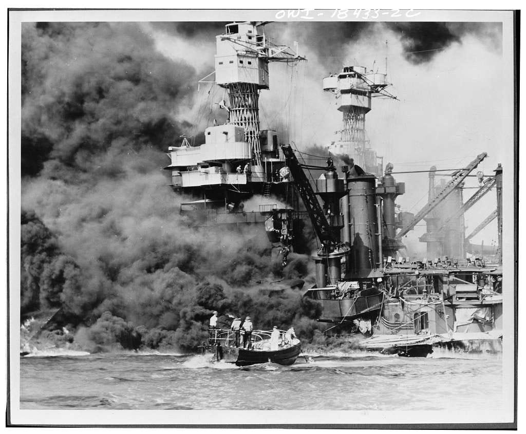 Black and white photo of a boat rescuing survivors from a battleship at Pearl Harbor