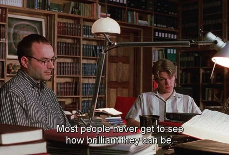 This may contain: two men sitting at a desk in front of books