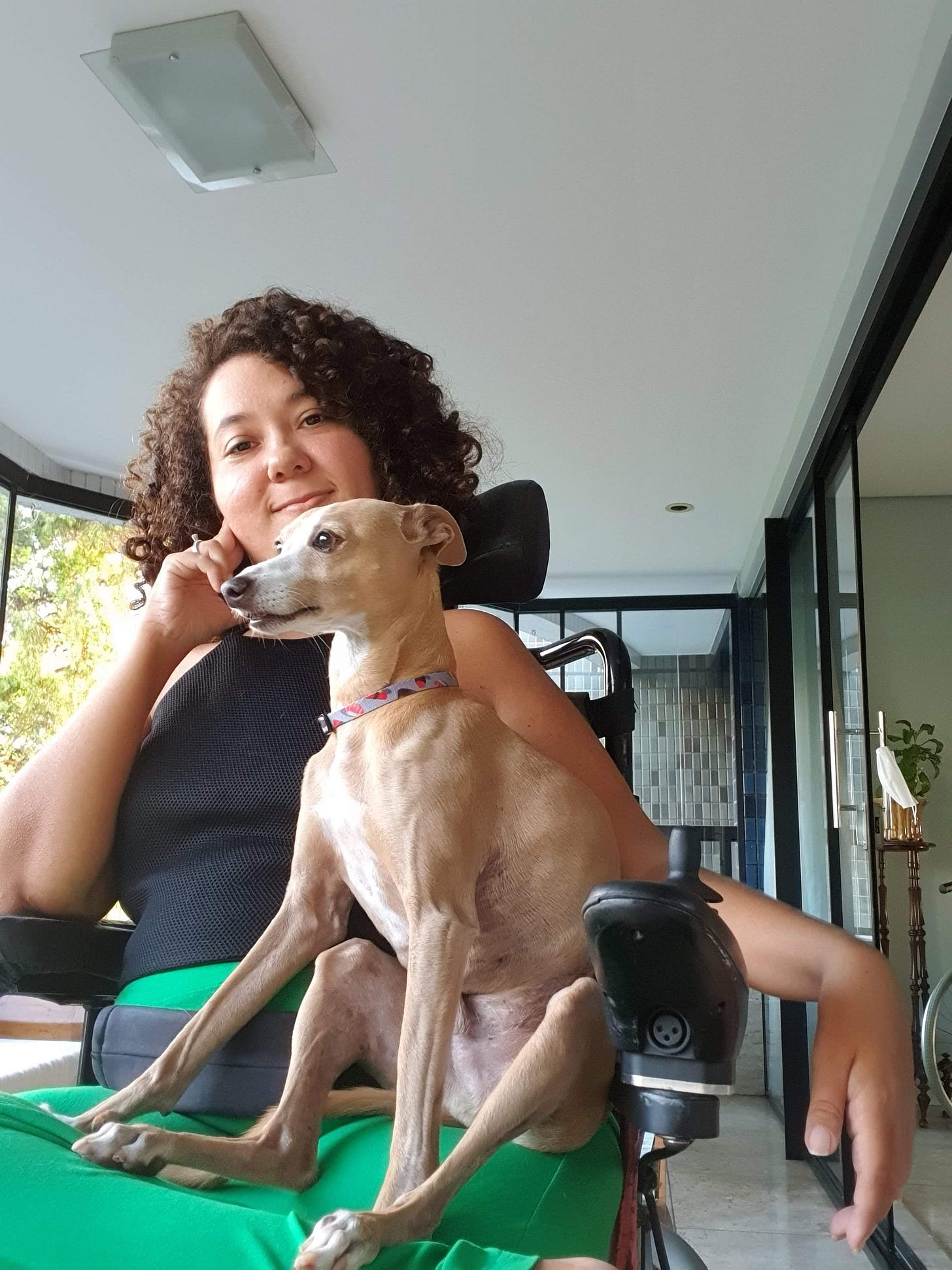 estou olhando para a camera, segurando meu rosto, sorrindo, vestindo preto e verde. ravi olha para o lado, sentado com as pernas de trás relaxadas, tem uma expressão sorridente 