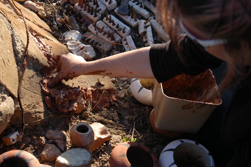 An archaeologist uses mud to patch holes in the kiln.