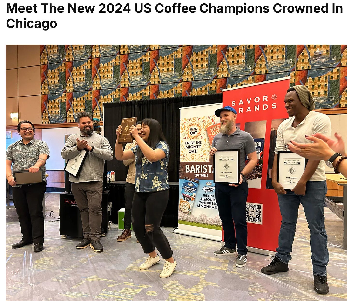 A woman holds up her winners plaque with a big smile while the runners up smile for the camera holding trophy plaques in a row behind her.