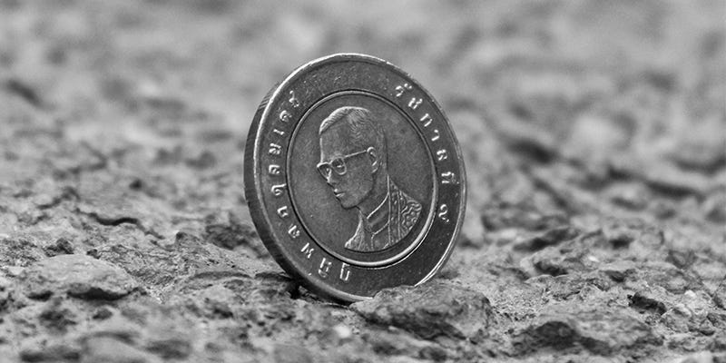 A coin with a face on it sits wedged on the stony ground