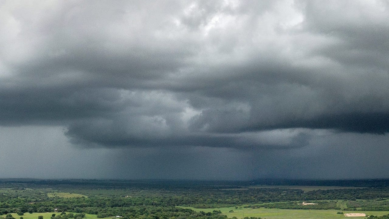 Dark rain clouds looming low over a green, wooded plain