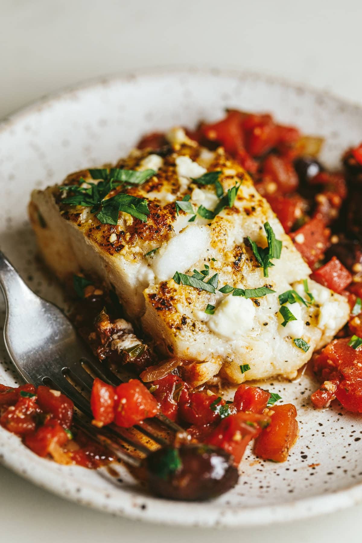 Mediterranean cod with tomatoes, Kalamata olives, and feta on a plate.