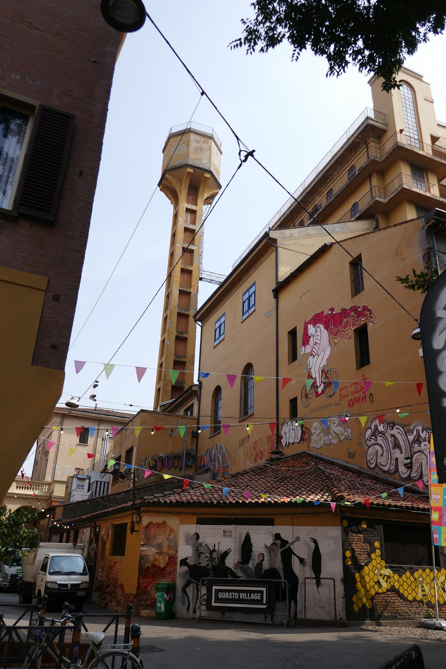 Guasto Village, with street art, colorful flags, and light strings against a castle-like building and watchtower